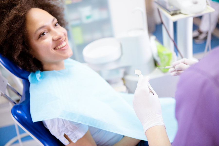 Curly-haired Black woman smiles while sitting in the dental chair talking to her dentist
