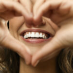 Closeup of a woman holding her hands in a heart shape over her beautiful smile