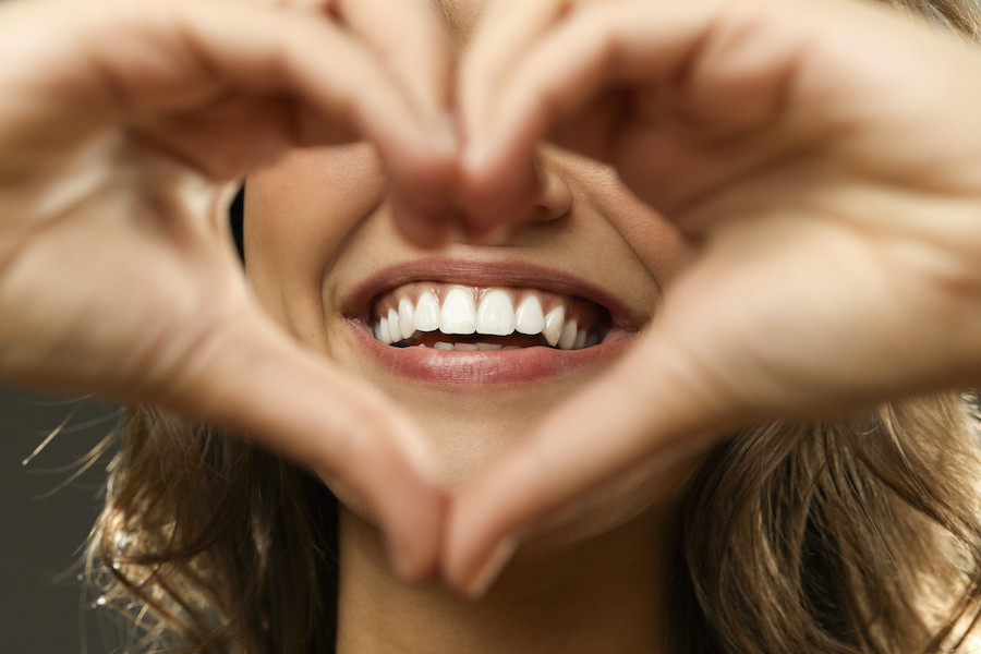 Closeup of a woman holding her hands in a heart shape over her beautiful smile