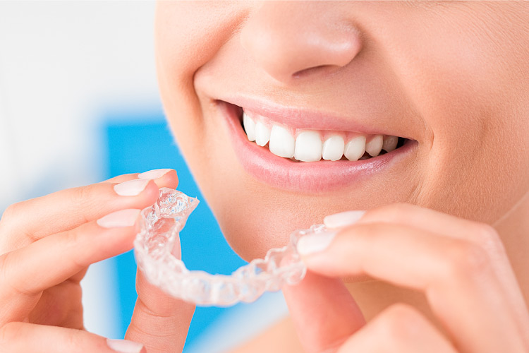 woman smiling holding up a clear aligner