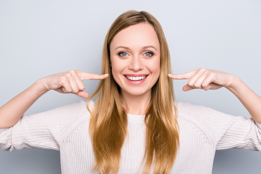 Blonde woman smiles and points horizontally to her white teeth